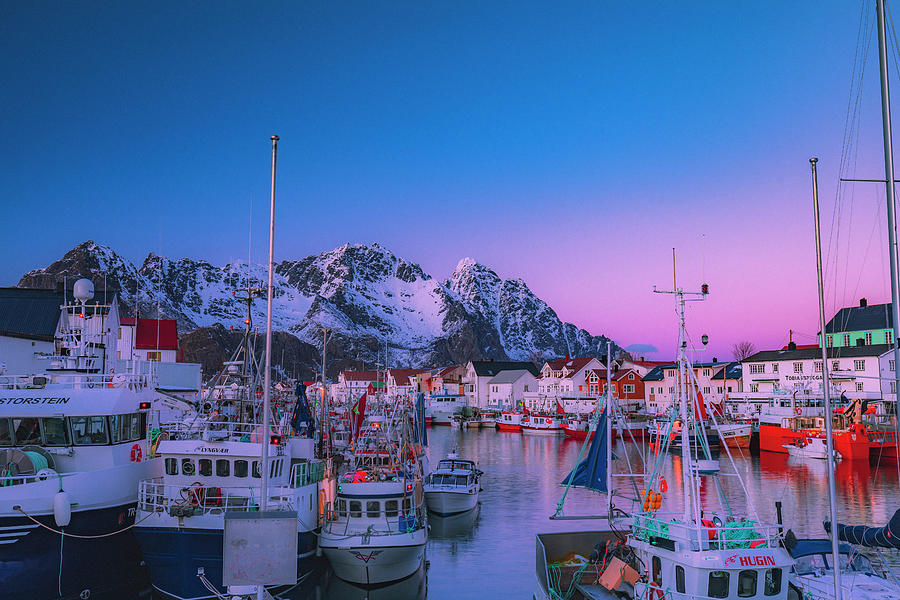 Norway, Nordland, Lofoten Islands, Henningsvaer, Scandinavia, The Fishing Village Of Henningsvaer At Dusk With The Boats In The Harbor And The Snow Capped Mountains In The Background Digital Art by Maurizio Rellini