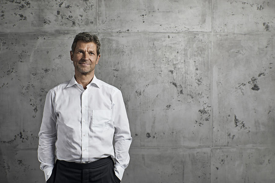 Portrait of smiling mature man in front of concrete wall #1 Photograph by Westend61