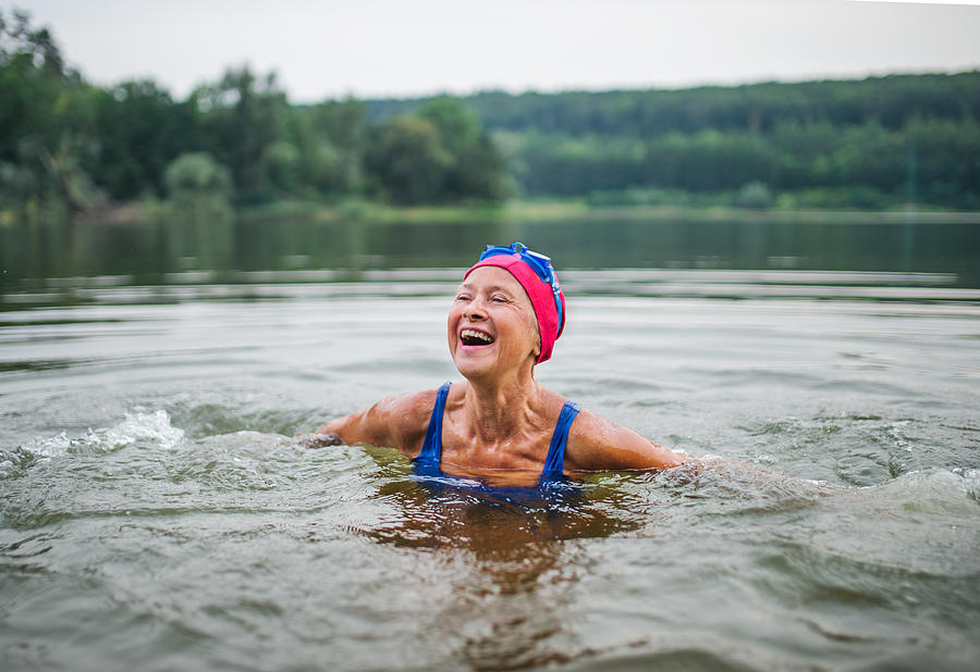 Active senior woman standing in lake outdoors in nature, laughing. Photograph by Halfpoint Images