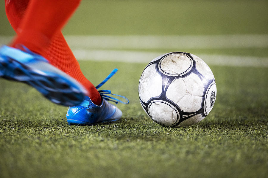 Athlete wearing cleats strikes a soccer ball on a grass field during a professional football match Photograph by Lighthouse Films