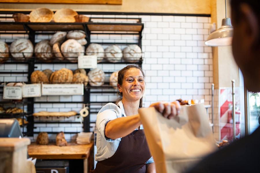 Bakery owner giving food package to customer Photograph by Alvarez
