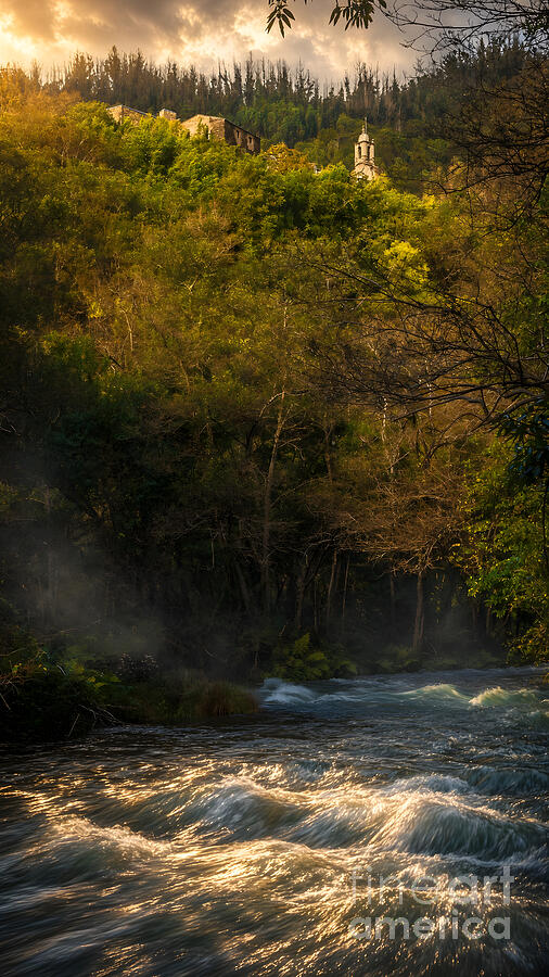 Sunlit river flowing through a forested gorge below the hilltop church tower of Caaveiro Monastery in the Fragas do Eume, Galicia, Spain