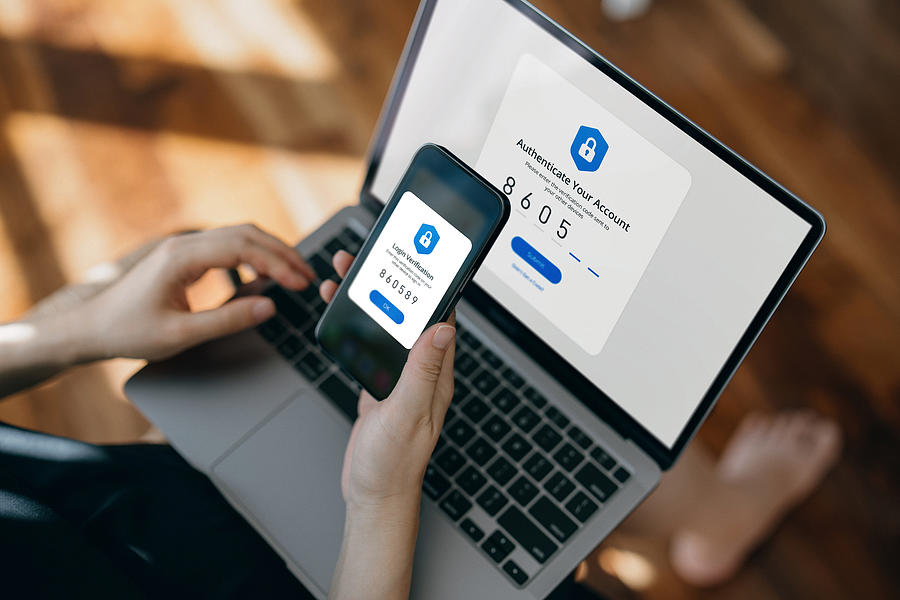 Cropped hand of woman using mobile device with Two-Factor Authentication (2FA) security while logging in securely to her laptop. Privacy protection, internet and mobile security Photograph by D3sign