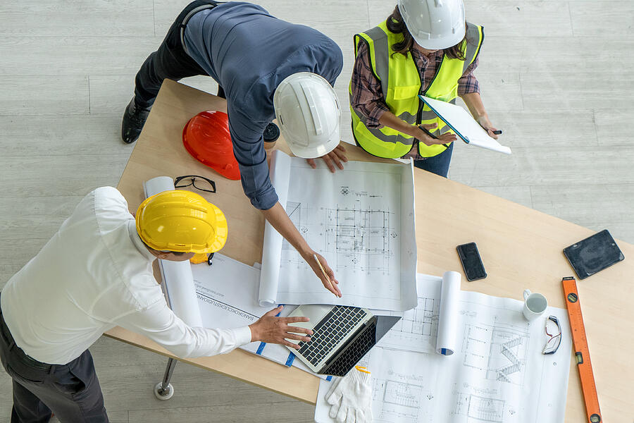 High Angle Photo From Directly Above Of An Architect A Businessman And A Construction Worker Examining A Blueprint On A Construction Site Boonchai Wedmakawand