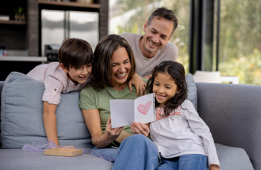 Loving family celebrating Mothers Day at home wih a beautiful card Photograph by Hispanolistic