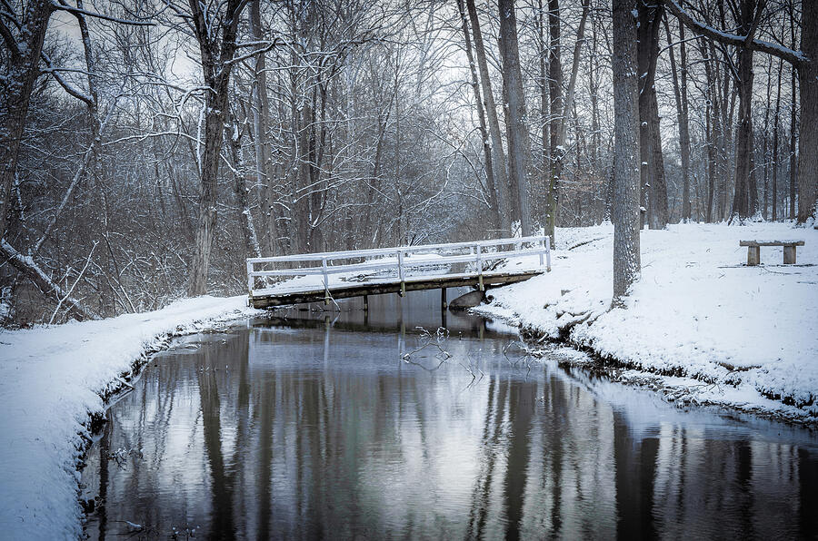 White pedestrian bridge crossing a dark creek in a snowy forest at Tawawa Park in Sidney Ohio