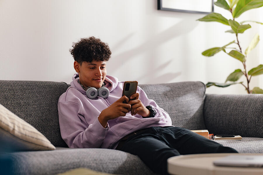 Teenage Boy with Smartphone Relaxing on Living Room Sofa Photograph by Miniseries