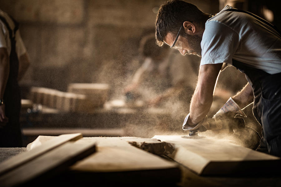 Young carpenter using sander while working on a piece of wood. Photograph by Skynesher
